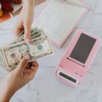A person handing dollar notes to another person with a pink payment terminal beside them.