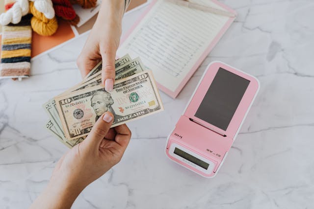 A person handing dollar notes to another person with a pink payment terminal beside them.